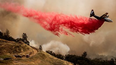 An airplane flies through a wildfire dropping fire retardant.