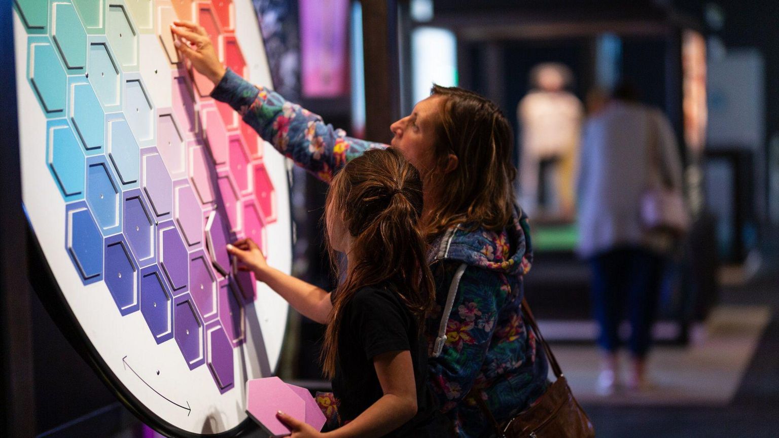 A woman and a girl placing hexagonal puzzle pieces on a board