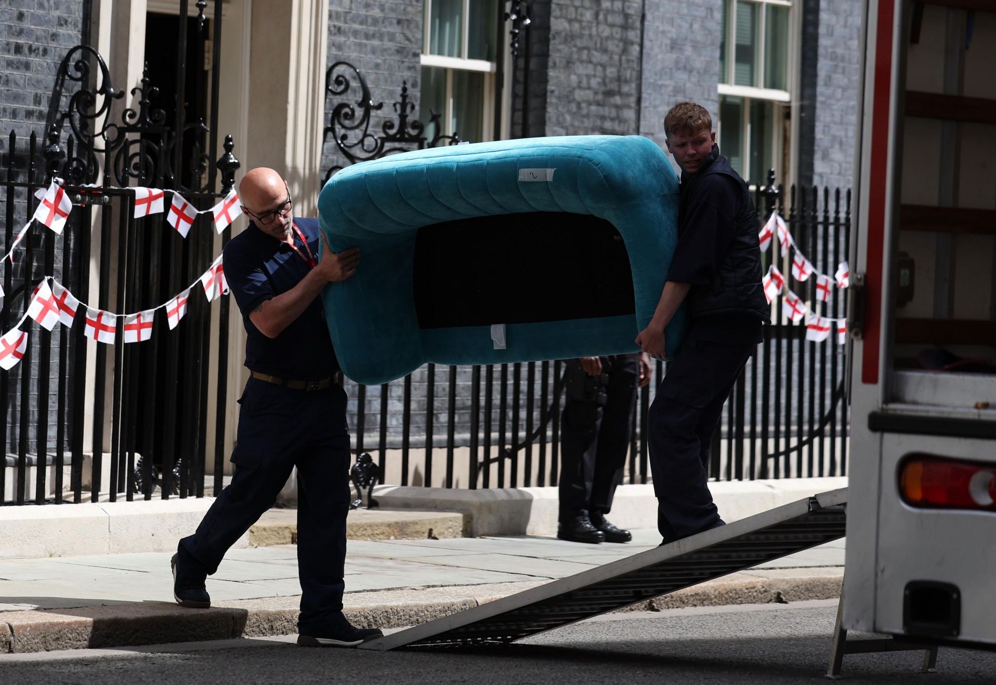 Two men carry a turquoise sofa into a van outside Downing Street