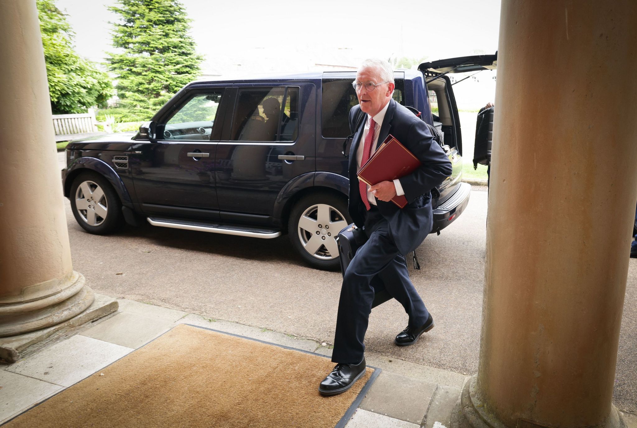 Hilary Benn walks past jeep and through pillars at entrance to Hillsborough Castle