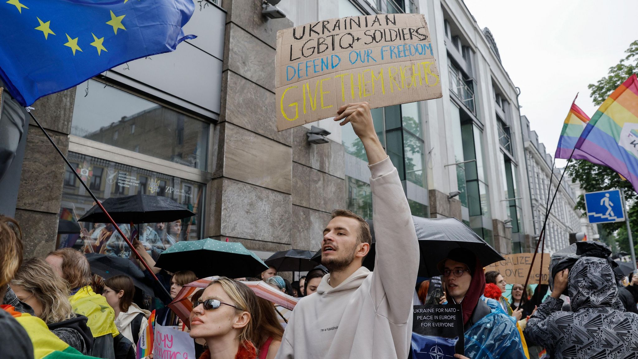 People at Pride march including a man holding a sign saying "Ukrainian LGBTQ soldiers defend our freedom - give them their rights"