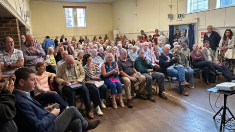 A meeting of residents in Bramley shows a room full of attendees and some standing around the edges of the hall