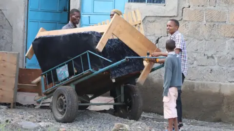 Family pushing a sofa on a wheelbarrow