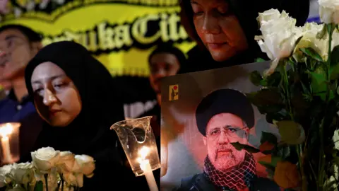 Reuters A woman holding a picture of the late Iranian President Ebrahim Raisi, attends a vigil to pay tribute to him and other victims who died in a helicopter crash, outside the Iranian embassy in Jakarta, Indonesia