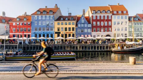 Alexander Spatari / Getty Images A cyclist passes a row of colourful houses