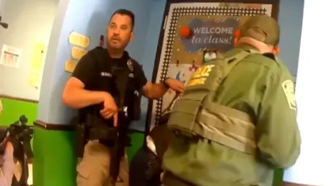 Two police officers are standing in front of a classroom door