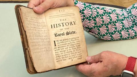 Two hands holding the top and bottom of a visibly worn book. The book is open. The pages are yellow.