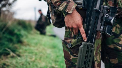 Close up view of a solider holding an assault rifle on a military training exercise in a rural location