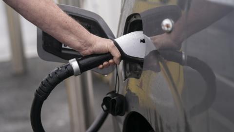 Close-up of a hand plugging in an EV charger into a grey car