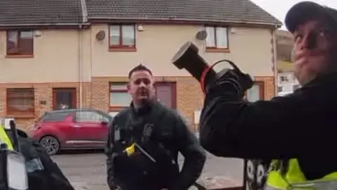 Three police officers on a street while one of them holds a battering ram above their head