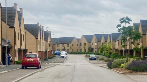 A road of newly-built homes, with cars parked alongside the pavement