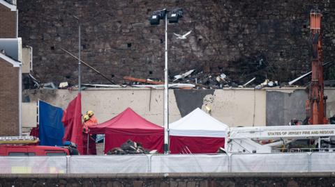 Scene of the Pier Road explosion, showing some rubble, tents erected by emergency services and some firefighters