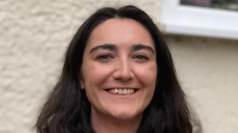 A close-up photograph of Saffron Roberts-Carey in which she is smiling while standing in front of her family's home