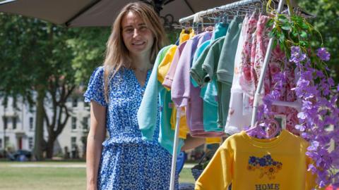 Tetyana stands next to a rail filled with colourful children's clothes