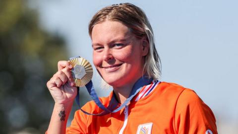 Sharon van Rouwendaal holds her gold medal up with a paw print tattoo on her wrist visible