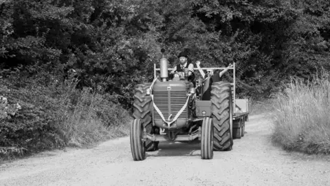 Paul Brewer A black and white styled image of a tractor travelling on a dirt road