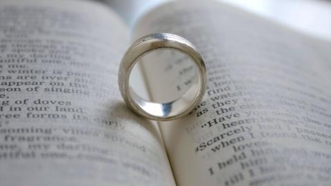 A wedding ring sits in the gutter of a bible.