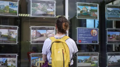 Woman looks at house adverts in a shop window