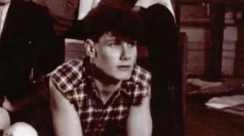 Sir Keir Starmer dressed in a checked shirt with cut-off sleeves props himself up on his arms next to a skull. His friends are posed around him.