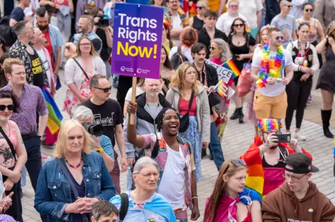 Man in parade holds sign saying Trans Rights Now 