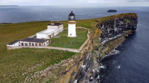 Aerial image of a white lighthouse, white two storey house and three outbuildings on a small island