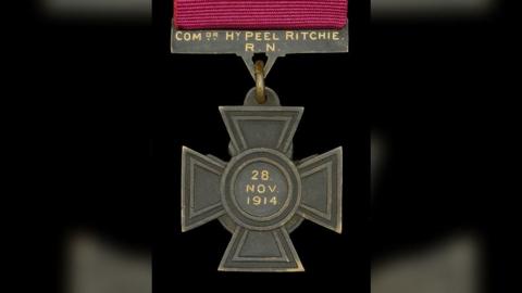 A cross-shaped medal with an inscription reading 'Comdr HY Peel Ritchie, 28 Nov 1914'