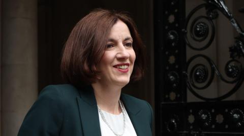 Bridget Phillipson smiles as she arrives for the first meeting of the Cabinet of the new Labour government in Downing Street. She has short brown hair, is wearing a dark green jacket, a white blouse and has a silver necklace.