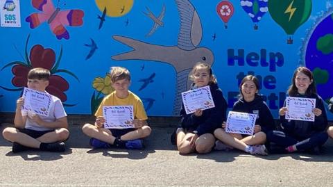 School students sitting in front of their artwork