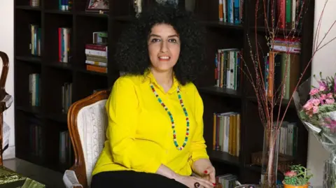 Narges Mohammadi, a jailed Iranian women's rights advocate, sitting down in front of a bookcase