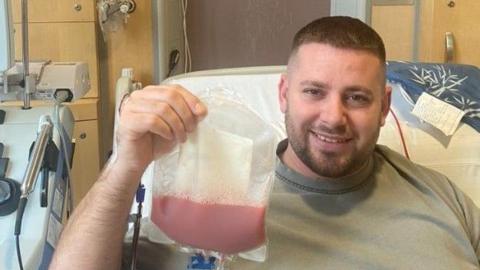 Nathan Brown with short brown hair and beard holds a bag of blood