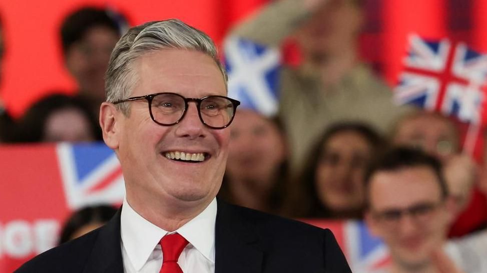 A smiling Sir Keir Starmer surrounded by cheering supporters, waving union jacks