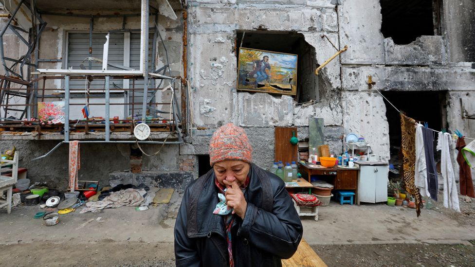 A woman reacts outside a damaged apartment building where she lives, Mariupol.