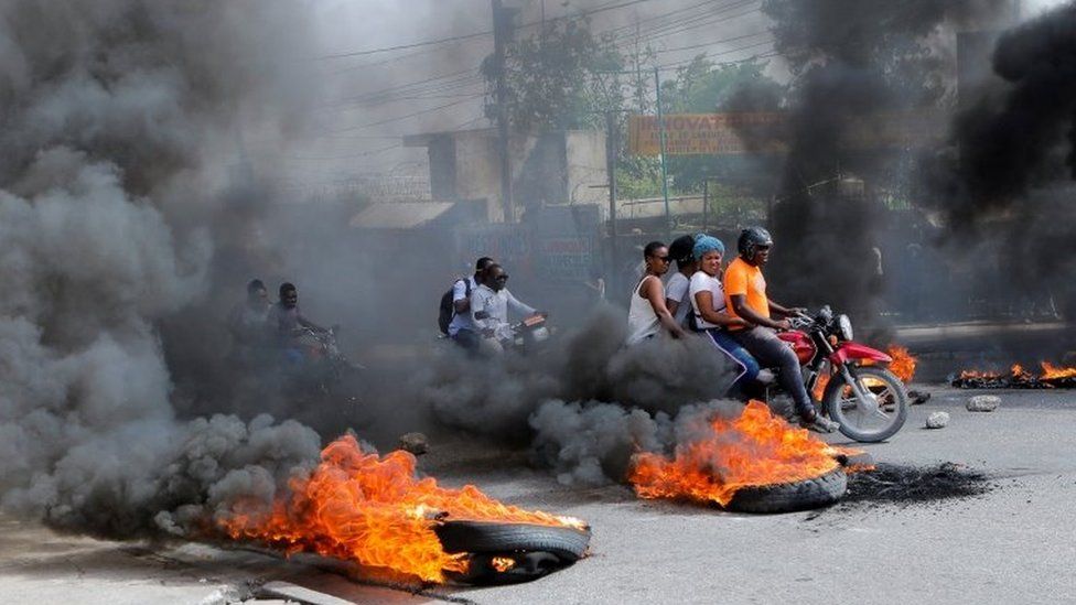 Motorcyclists with passengers drive past burning tyres in Port-au-Prince, Haiti. Photo: 13 July 2022