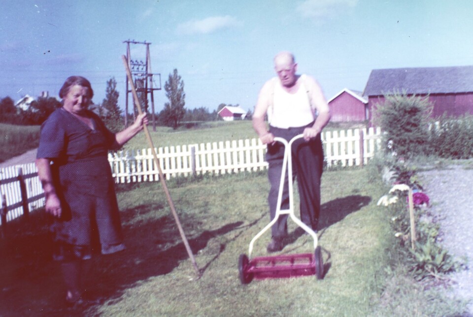 En mann og en kvinne gjør hagearbeid rundt 1960. Mannen bruker en manuell gressklipper. Kvinnen poserer med en rake.