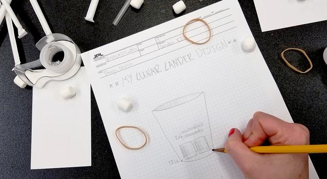 Sketch of a lunar lander on graph paper with marshmallows, rubber bands and straws scattered around