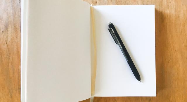 An open journal and a pen on a wood table.