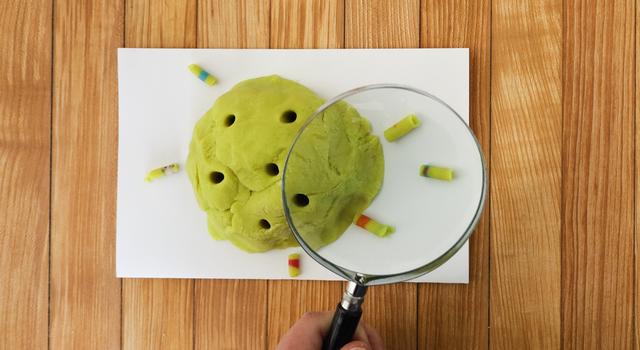 A person holds a magnifying glass over their play dough rock cores