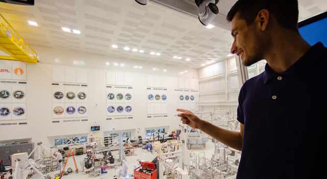 Adrien Dias-Ribiero stands in the gallery above the clean room at JPL and points down at engineers in building the Mars 2020 rover.