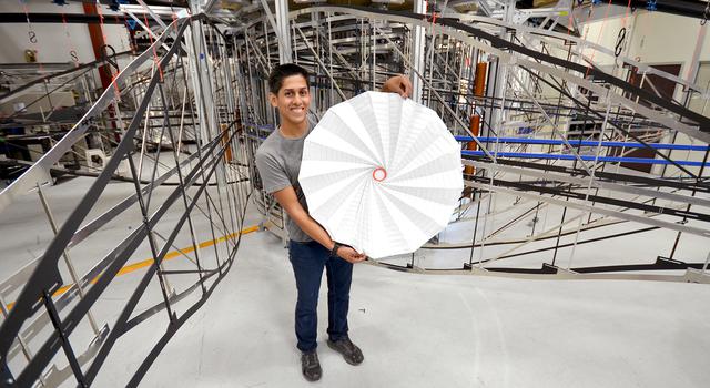 JPL Christopher Esquer-Rosas holds an origami version of the Starshade engineering model behind him.