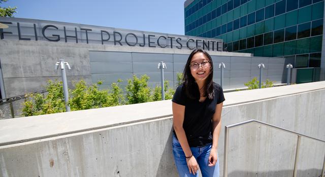 Tiffany Shi poses for a photo in front of a steel and glass building at JPL with the words "Flight Projects Center" displayed on the front of the building.