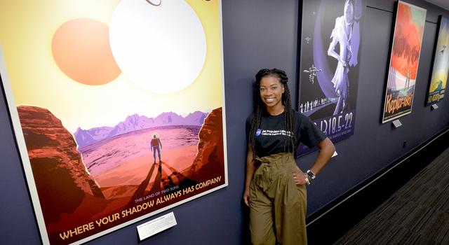 JPL intern Tre'Shunda James stands in front of NASA's "Visions of the Future" posters