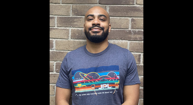 Yohn Ellis wears a JPL shirt and poses in front of a brick wall.