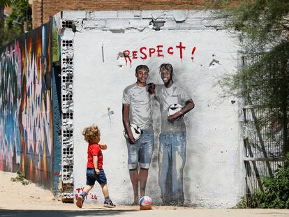 Un niño juega con una pelota junto a un mural de Lamine Yamal y Nico Williams en Barcelona.