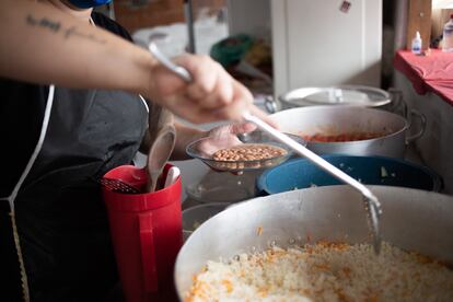 Um auxiliar de cozinha trabalha com Pai Ronaldo e voluntários ajudam a distribuir as marmitas.