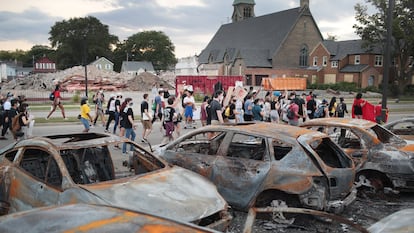 Um grupo de manifestantes pacíficos passa por carros queimados em Kenosha.