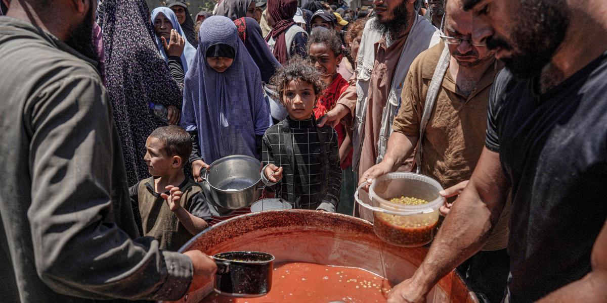 Personas se reparten porciones de comida de una gran olla en una cocina pública de Deir el-Balah, en el centro de la Franja de Gaza.