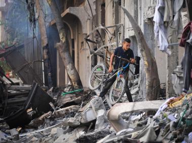 Un niño palestino carga su bicicleta mientras trepa por los escombros un día después de una operación de las Fuerzas Especiales israelíes en el campamento de Nuseirat, en el centro de la Franja de Gaza,