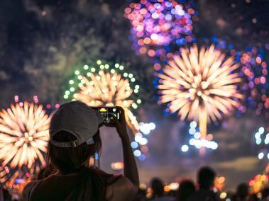 The back of a girl in a baseball cap filming a fireworks display on her mobile phone