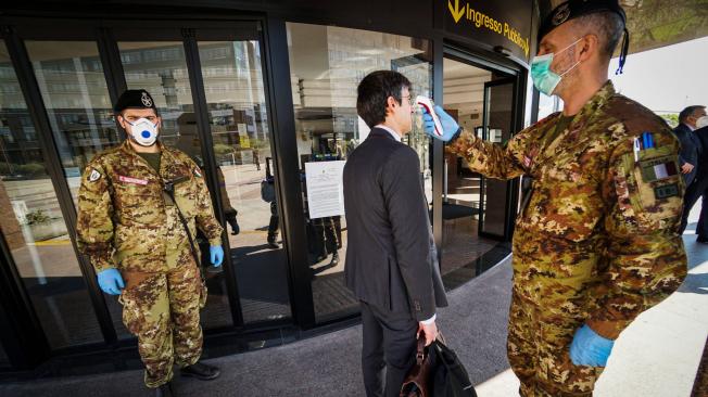 En la puerta de entrada a una Corte de Nápoles (Italia) militares le toman la temperatura a una persona en traje que pretende ingresar al sitio.