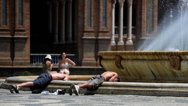 Dos jóvenes sumergen la cabeza en el agua de una fuente para refrescarse, en la Plaza de España de Sevilla.